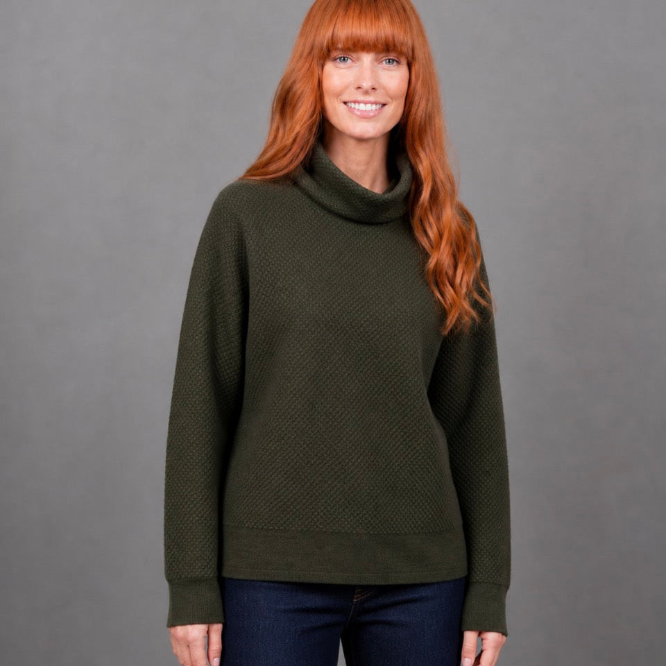 Woman wearing the Ball stitch high crew green jumper in Olive by Bridge and Lord